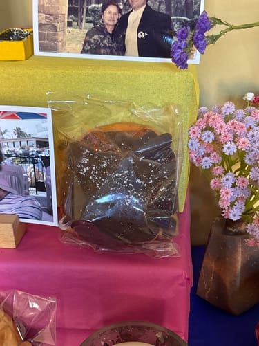 Customer's Pan de Muerto in a clear plastic bag, placed on a decorative altar with flowers and photographs.