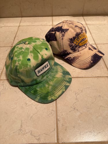 Customer's custom dyed Heritage Canvas Caps sitting on a tiled surface, showing green tie-dye and bleached patterns.