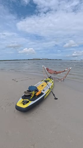 Reviewer's Go Hammock set up on a sandy beach next to a yellow and black paddleboard with the ocean in the background.