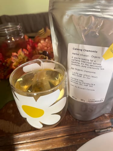 Customer's Calming Chamomile tea in a clear glass cup with a white daisy pattern, alongside the tea packaging.
