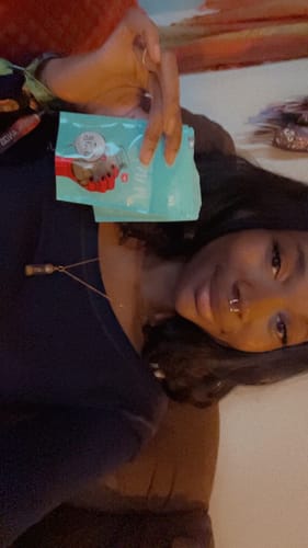Customer's hand holding a turquoise pouch of Lazy OG Greenhouse CBD Flower.