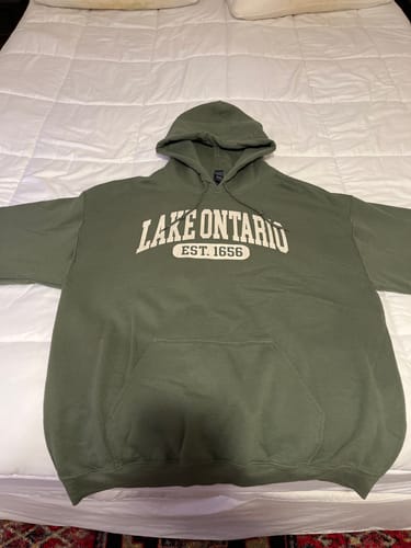 Customer's olive green Lake Ontario hoodie laid flat on a white bedspread.