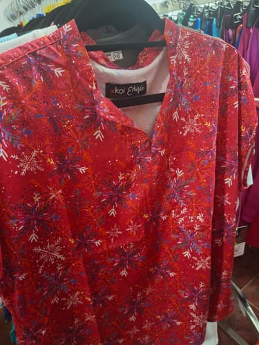 Customer's Koi 1093PRA EVS top with festive red snowflake print hanging on a black hanger.