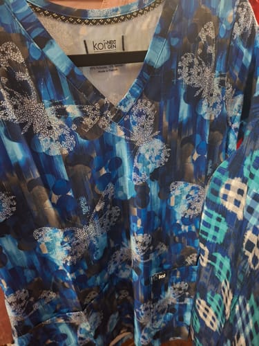 Reviewer's Koi 1029PR top with blue butterfly print, showing the V-neck and front pocket detail.