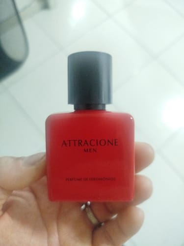Customer's hand holding the bright red Attracione Men perfume bottle with black cap.