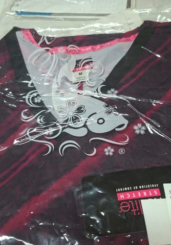 Customer's Koi 1071PR top in original clear packaging, featuring a dark floral print and a soft fabric label.
