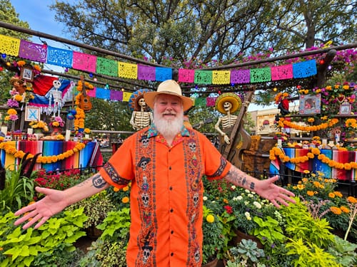 Customer's orange Que Vivan Los Muertos Guayabera worn at a sunny Disneyland event with festive decor.
