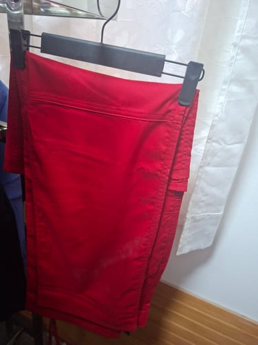 Reviewer's Cherokee Revolution pantalón clínico rojo colgado en un gancho, mostrando su diseño y color.