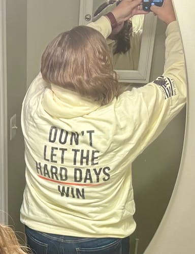 Customer wearing the soft, light-yellow Hard Days hoodie, showcasing the back text design in a mirror reflection.