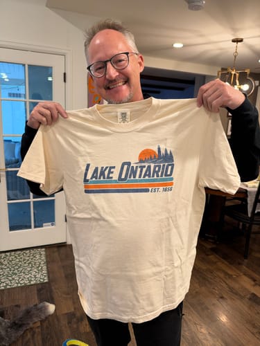 Customer's cream Lake Ontario Retro Stripe T-Shirt, held up in a home setting.