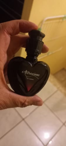 Customer's hand holding a black heart-shaped Attracione Sensual perfume bottle with elegant white text.