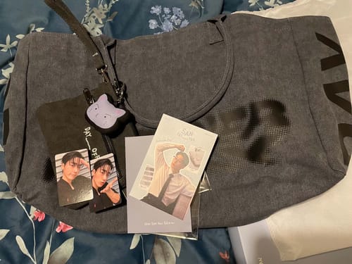 Customer's SAN DAY OFF merch including a grey tote bag, small zippered pouch, character keyring, and two photo cards.