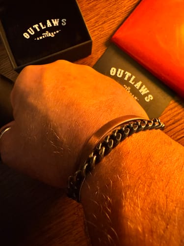 Customer's Enforcer Bracelet worn on a wrist, featuring a dark metal chain design with branded gift boxes in the background
