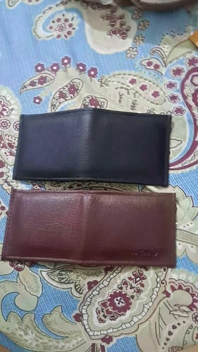 Customer's two plain black and brown wallets lying on a patterned fabric surface.