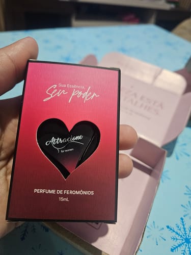 Customer's hand holding the Perfume Attracione Sensual box with a heart-shaped cutout against an open shipping box.