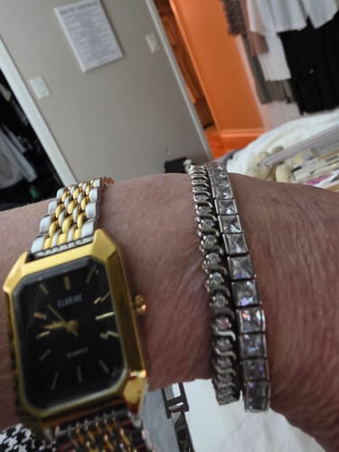 Customer's gold and silver-toned Claire De Mains watch worn on a wrist next to a sparkling tennis bracelet.