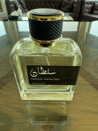 Customer's Sultan perfume bottle with a black textured cap, sitting on a glossy wooden table.