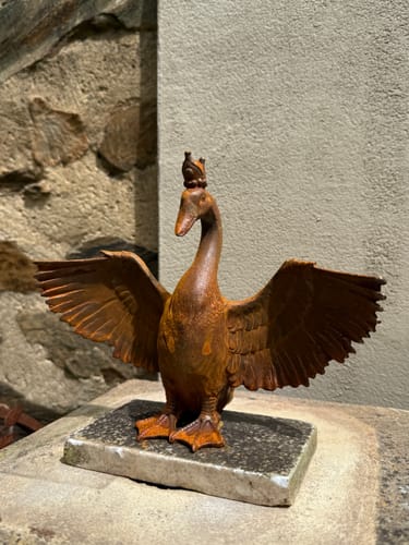 Customer's Princess Evangeline rust-colored cast iron goose statue with outstretched wings, displayed on stone.