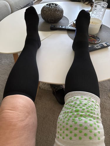Kundens svarta Diasocks stödstrumpor på benen, uppdragna till knäna, medan personen sitter vid ett bord.
