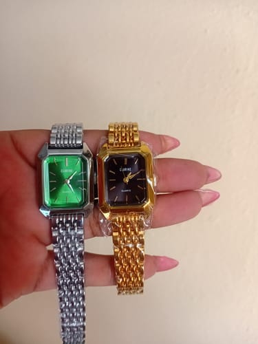 Customer's hand holding a silver and a gold Claire De Mains watch, both featuring rectangular faces.