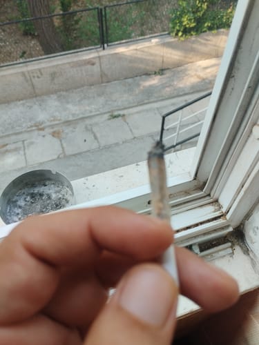 Customer's hand holding a lit joint of Cali Mix AAA+ premium flower, with an ashtray nearby.