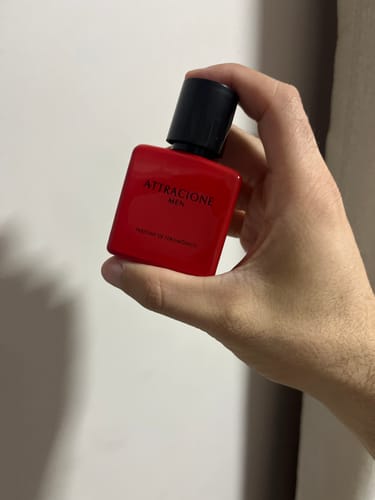 Customer's hand holding a square red Attracione Men perfume bottle with a black cap.