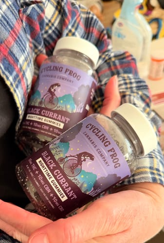 Customer's hands holding two bottles of Cycling Frog Black Currant Nighttime Gummies.