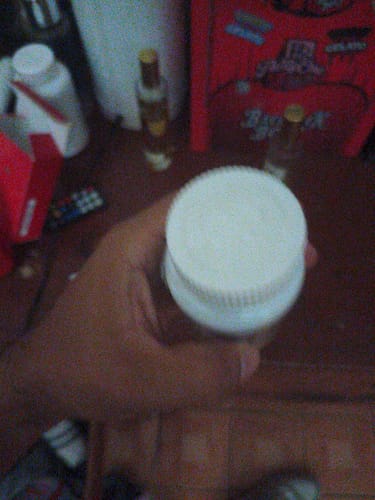 Customer's hand holding a white bottle of Clomibol, with other bottles blurred in the background.