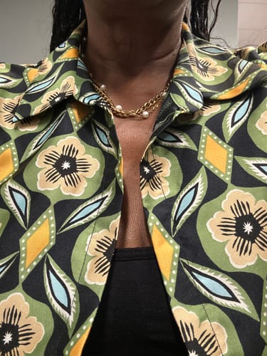 Customer's gold-tone Santorini Pearl Necklace worn around the neck, styled with a patterned green floral shirt.