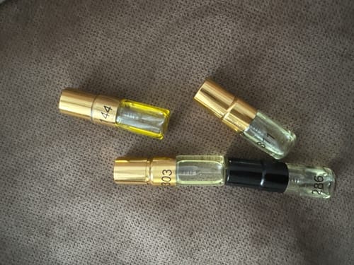 Kundenfoto vom Tester Set mit vier kleinen Parfümproben in Glasfläschchen mit goldenen Deckeln auf einem braunen Untergrund.