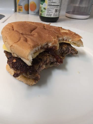 Customer's bitten Halal Gourmet Beef Burger on a white plate with sauce inside.