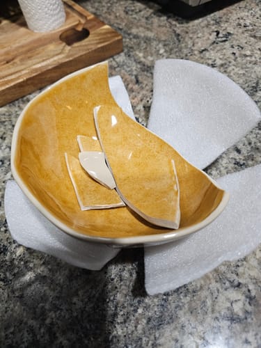 Customer's broken amber Sunstone bowl from the 16-Piece Organic Dinnerware Set, sitting on a granite countertop.