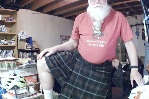 Reviewer wearing a coral-colored Down With Pants Up With Kilts T-shirt featuring a frog graphic, paired with a plaid kilt.
