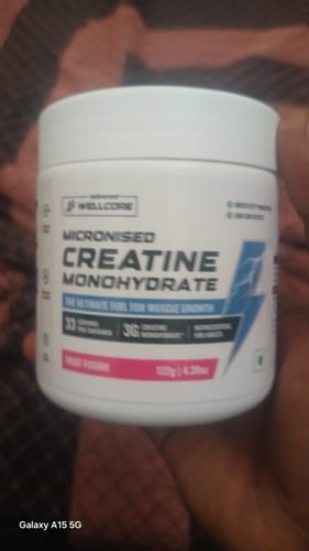 Reviewer's hand holding a white tub of Wellcore Micronised Creatine Monohydrate, Fruit Fusion flavor.