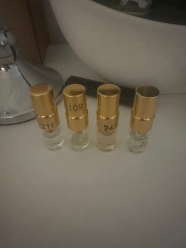 Kunde zeigt vier kleine Tester Set Parfümfläschchen mit goldenen Kappen auf einer hellen Oberfläche.