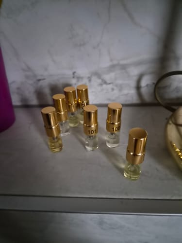 Customer's Tester Set with several small, clear fragrance vials featuring gold caps arranged on a marble surface.