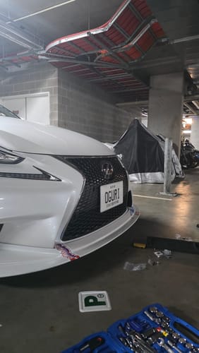 Customer's JDM Plate Bracket installed on the front bumper of a white car in a parking garage.