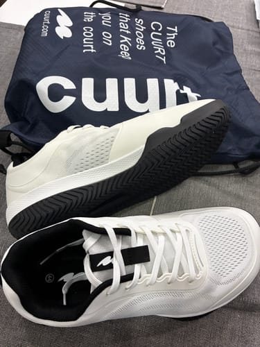 Customer's white and black CUURT Muuv court shoes and branded drawstring bag on gray fabric surface.