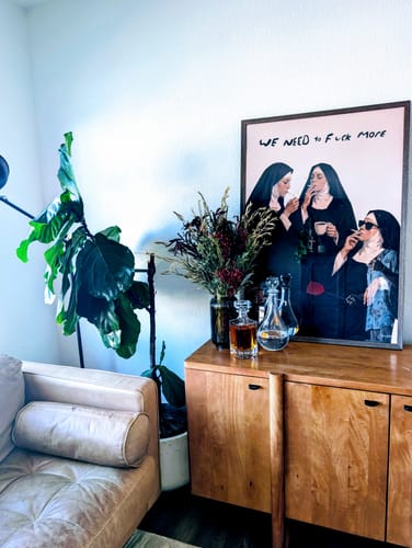 Customer's Out Of Office art print, framed on a wooden sideboard next to a large plant.