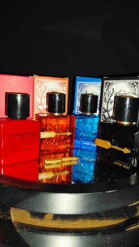 Customer's Kit Adonis and Attracione Men fragrance bottles arranged with colorful boxes on a reflective surface.