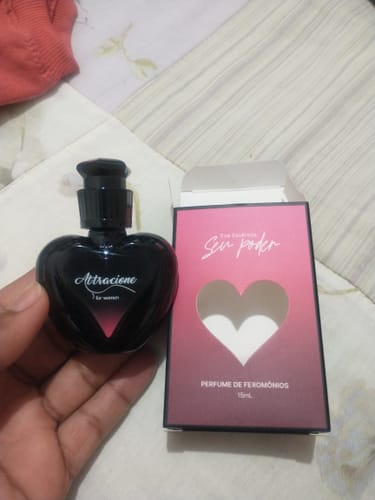 Reviewer's hand holding a heart-shaped Attracione perfume bottle next to its pink and black box.