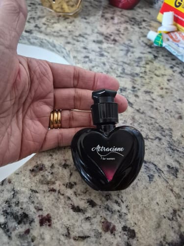 Customer's Attracione Feminino perfume in a heart-shaped black bottle held in a hand.
