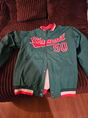 Customer's green varsity jacket with Hawaii and number 50 on the chest, lying on a brown sofa.