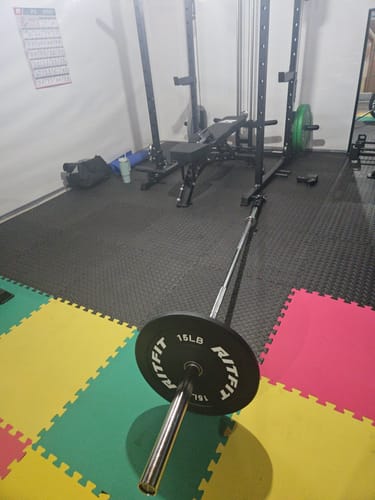 Customer's home gym setup featuring a weight rack with a Ritfit 15lb barbell plate in the foreground.