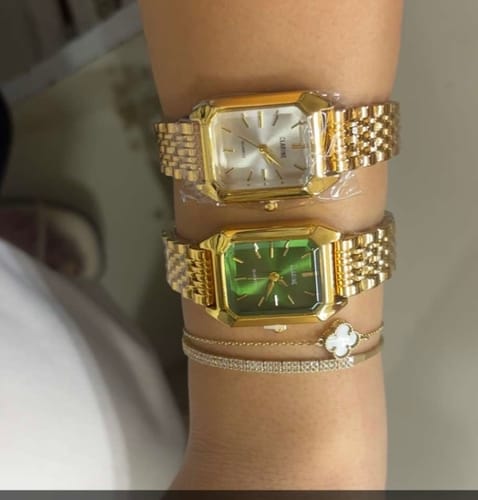 Customer's wrist wearing two Claire De Mains gold watches with link bracelets, one with white and one with green faces.