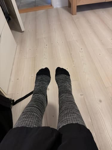 Reviewer's legs wearing patterned grey and black Diasocks støttestrømper while sitting indoors.