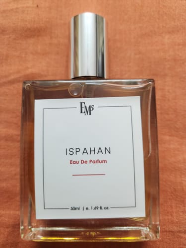 Customer's 50ml bottle of Ispahan Eau De Parfum, shown centered on a textured, amber-toned fabric background.
