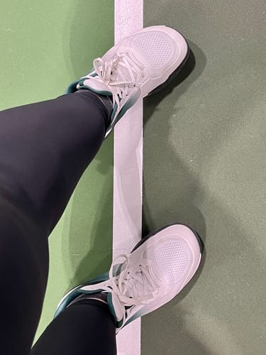 Customer's white CUURT Muuv court shoes being worn on a green athletic court.