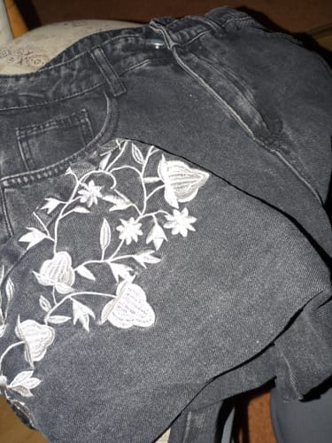 Reviewer's black denim jeans featuring detailed white floral embroidery on the pocket area.