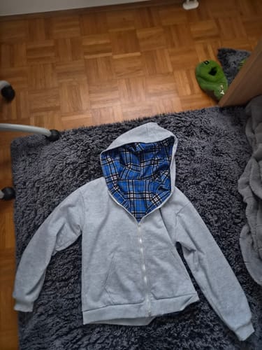 Reviewer's gray Sweat Plaid Réversible hoodie laid flat on a gray rug, revealing the blue plaid hood lining.